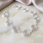 Open silver spiral bracelet on light wood background, handmade UK jewellery