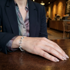 Person wearing a silver bracelet on a wooden table in a blurred indoor setting