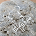Silver spiral earrings on a textured stone surface
