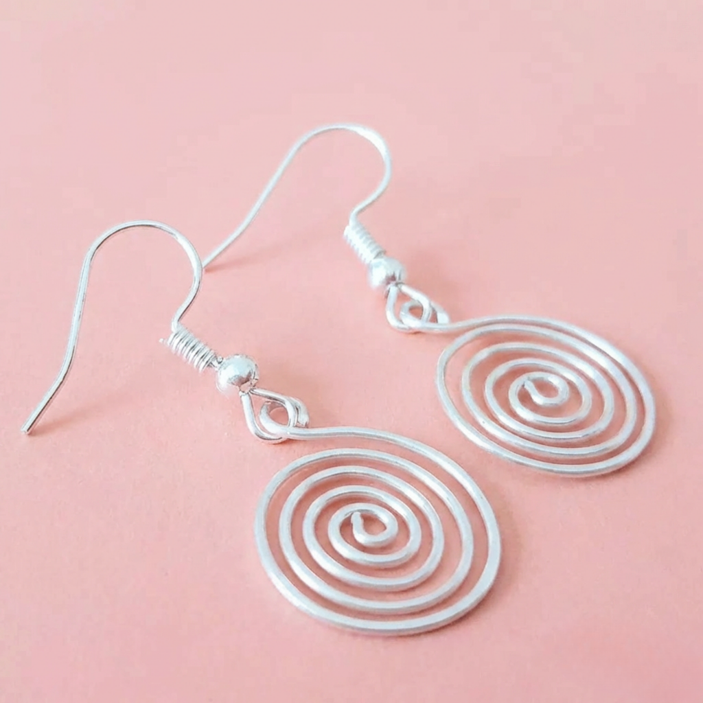 Silver spiral earrings on a pink background
