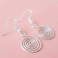 Silver spiral earrings on a pink background