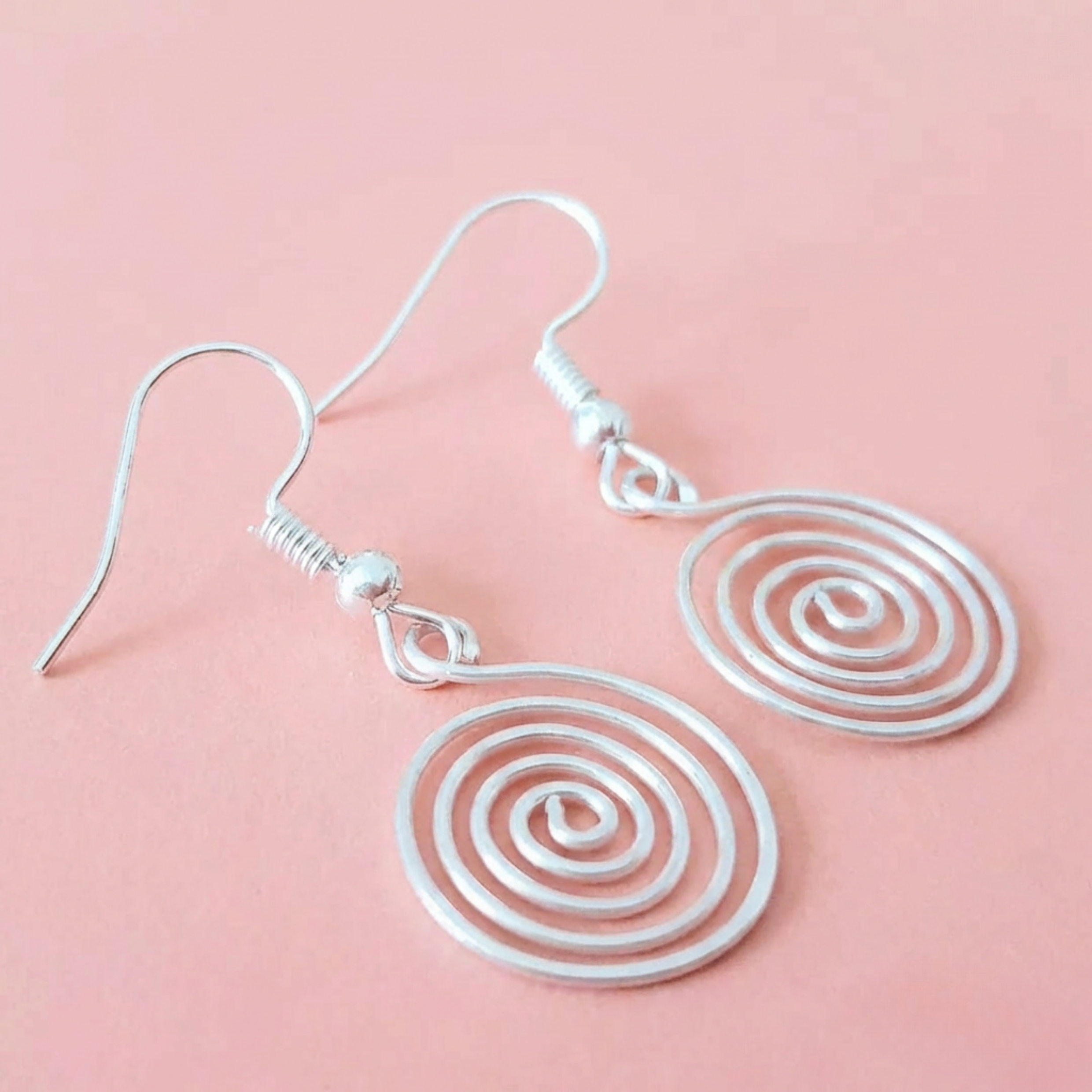 Silver spiral earrings on a pink background