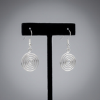 Silver spiral earrings on a black earring stand against a gray background