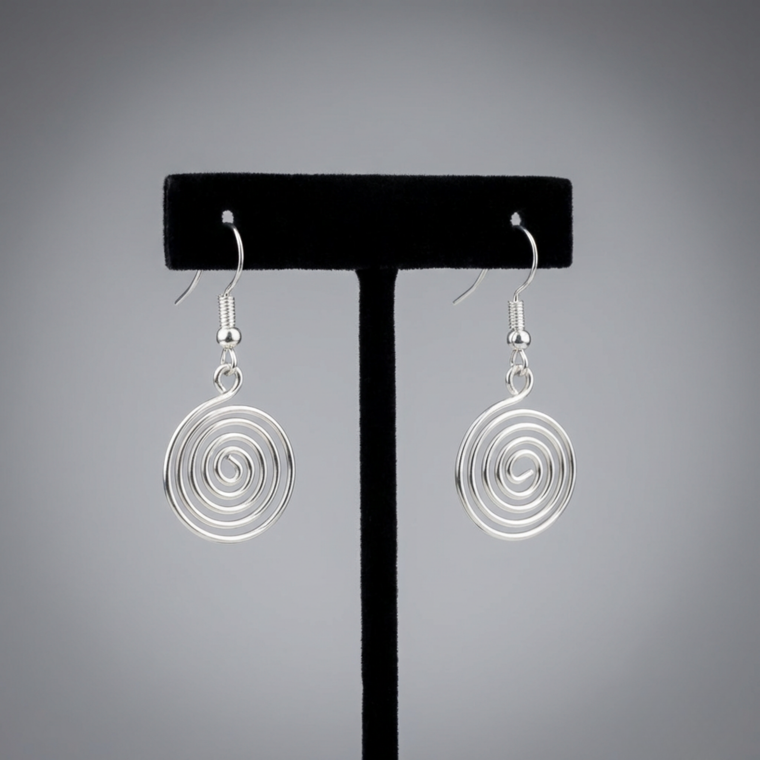 Silver spiral earrings on a black earring stand against a gray background
