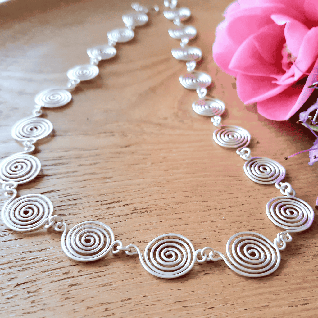 Silver spiral necklace on a wooden surface with a pink flower