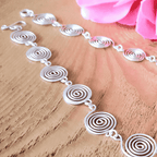 Silver spiral necklace on a wooden surface with pink flowers in the background