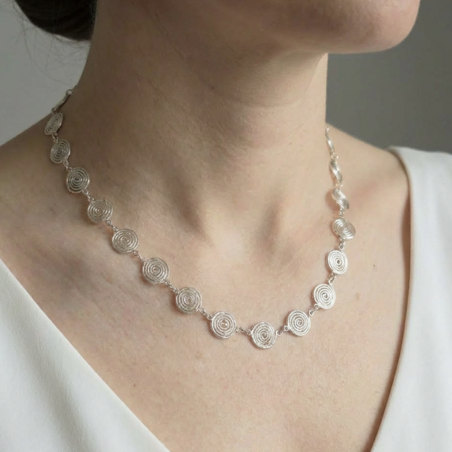 Silver spiral necklace with circular design worn by a person against a neutral background