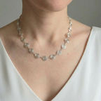Necklace with silver circular spirals worn by a person in a white top against a neutral background
