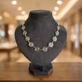 Silver spiral necklace on a black mannequin bust with a blurred indoor background