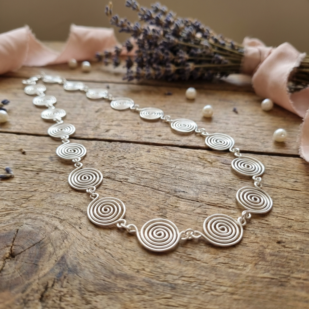 Silver spiral necklace on a wooden surface with lavender and ribbons.