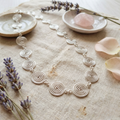 Silver necklace with circular design on a textured surface with lavender and rose petals.