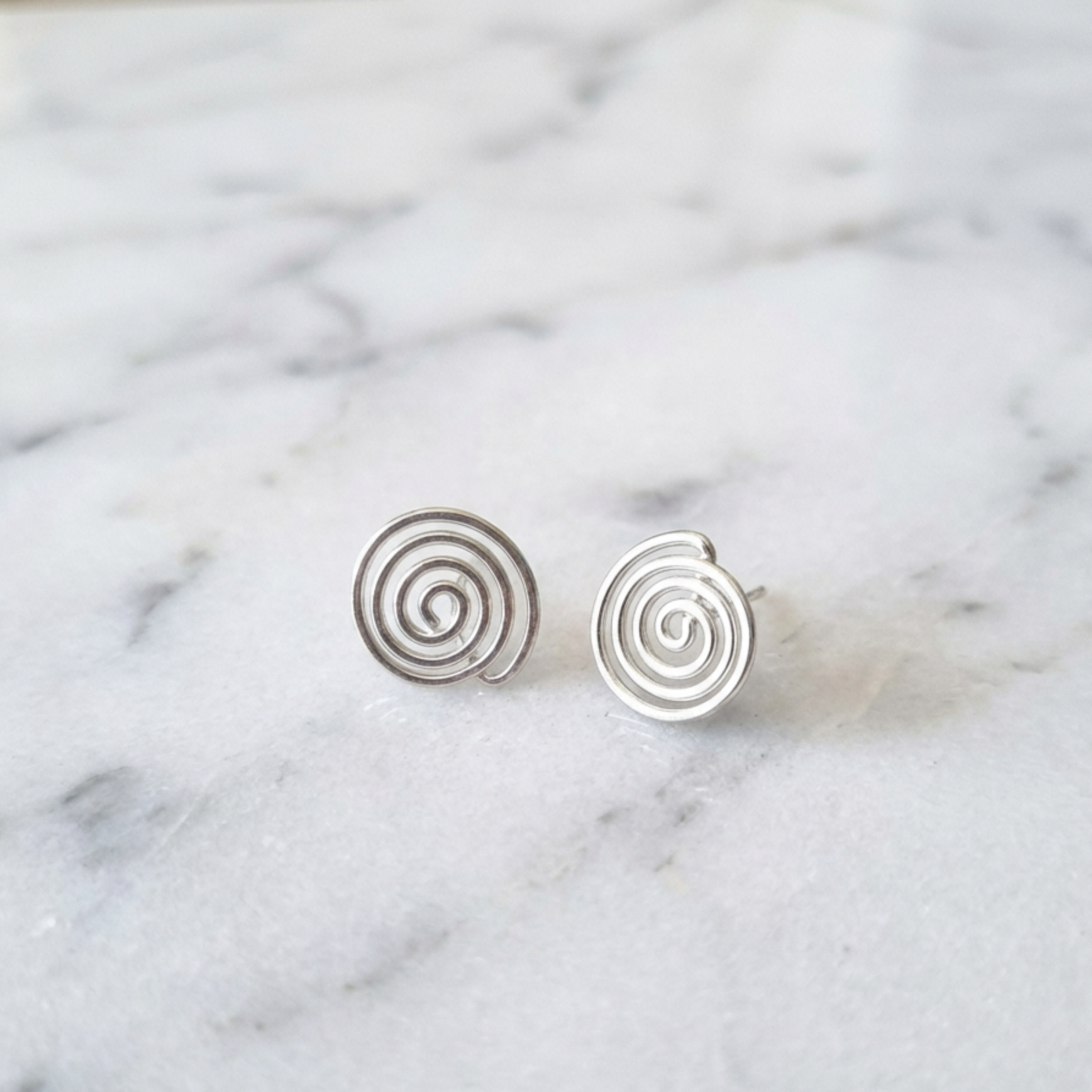 Silver spiral earrings on a marble background