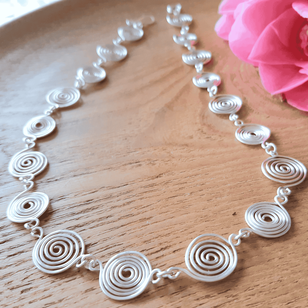 Silver spiral necklace on a wooden surface with a pink flower