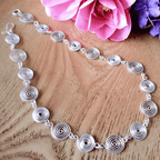 Silver necklace with circular design on a wooden surface with pink flowers.