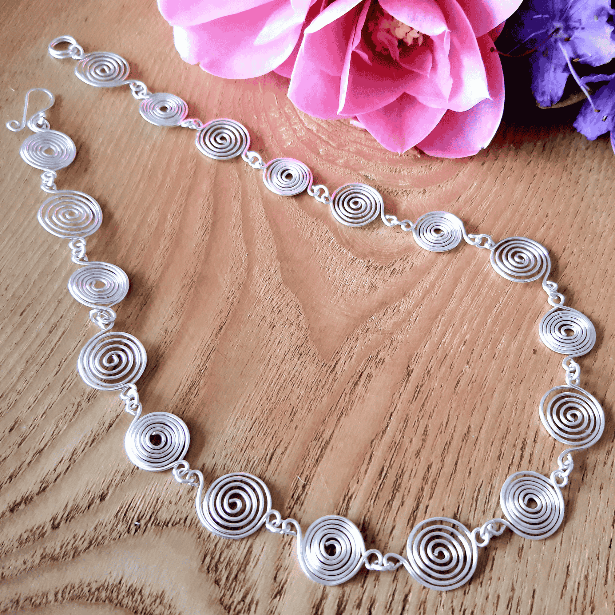 Silver necklace with circular design on a wooden surface with pink flowers.