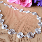 Silver spiral necklace on a wooden surface with pink flowers in the background