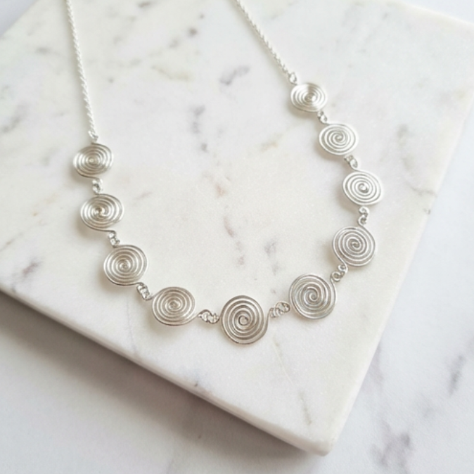 Silver necklace with circular design on a marble surface