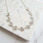 Silver necklace with circular design on a marble surface