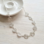 Silver spiral necklace on a light wooden surface with a white dish in the background.