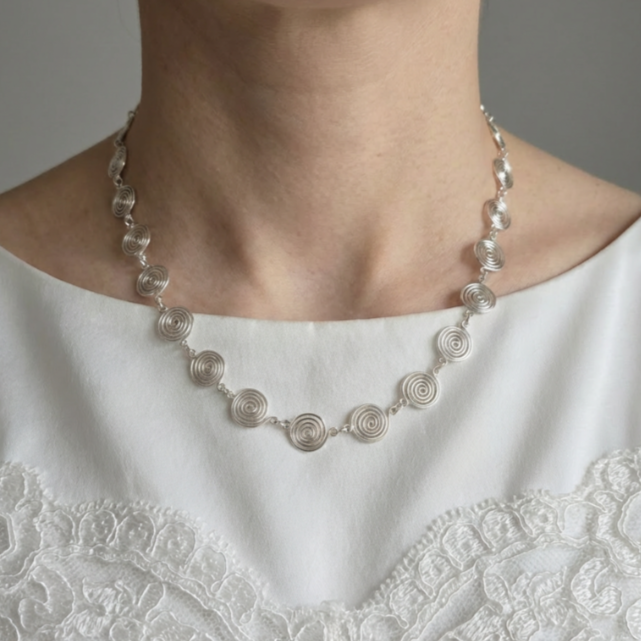 Silver spiral necklace worn by a person in a white lace garment