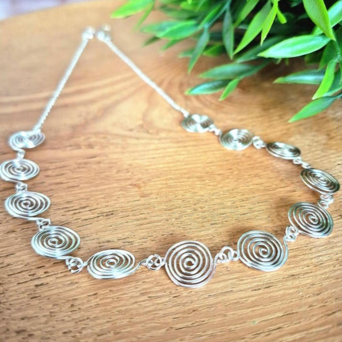 Silver spiral necklace with chain on a wooden surface with green leaves in the background