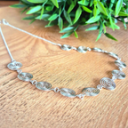 Silver necklace with spiral design on a wooden surface with green leaves in the background