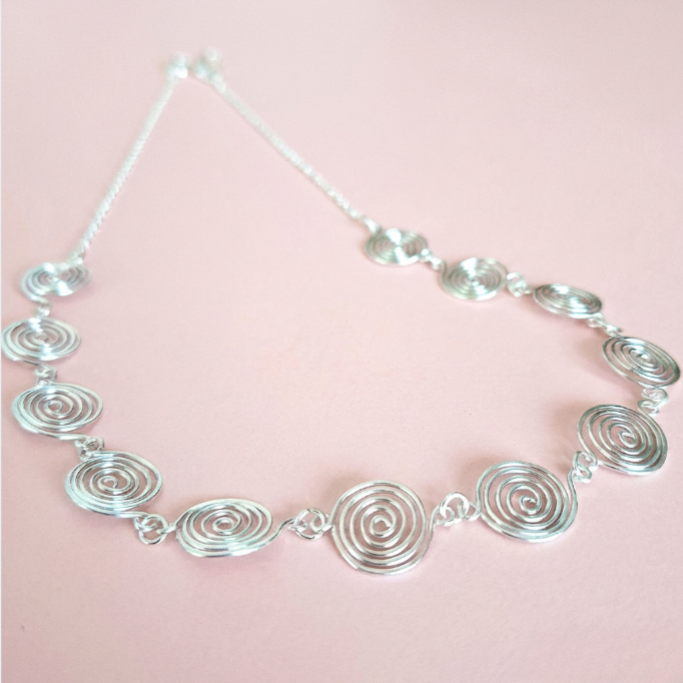 Silver spiral necklace on a pink background