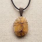 Copper Tree of Life encasing a orange calcite stone pendant on a cream fabric surface