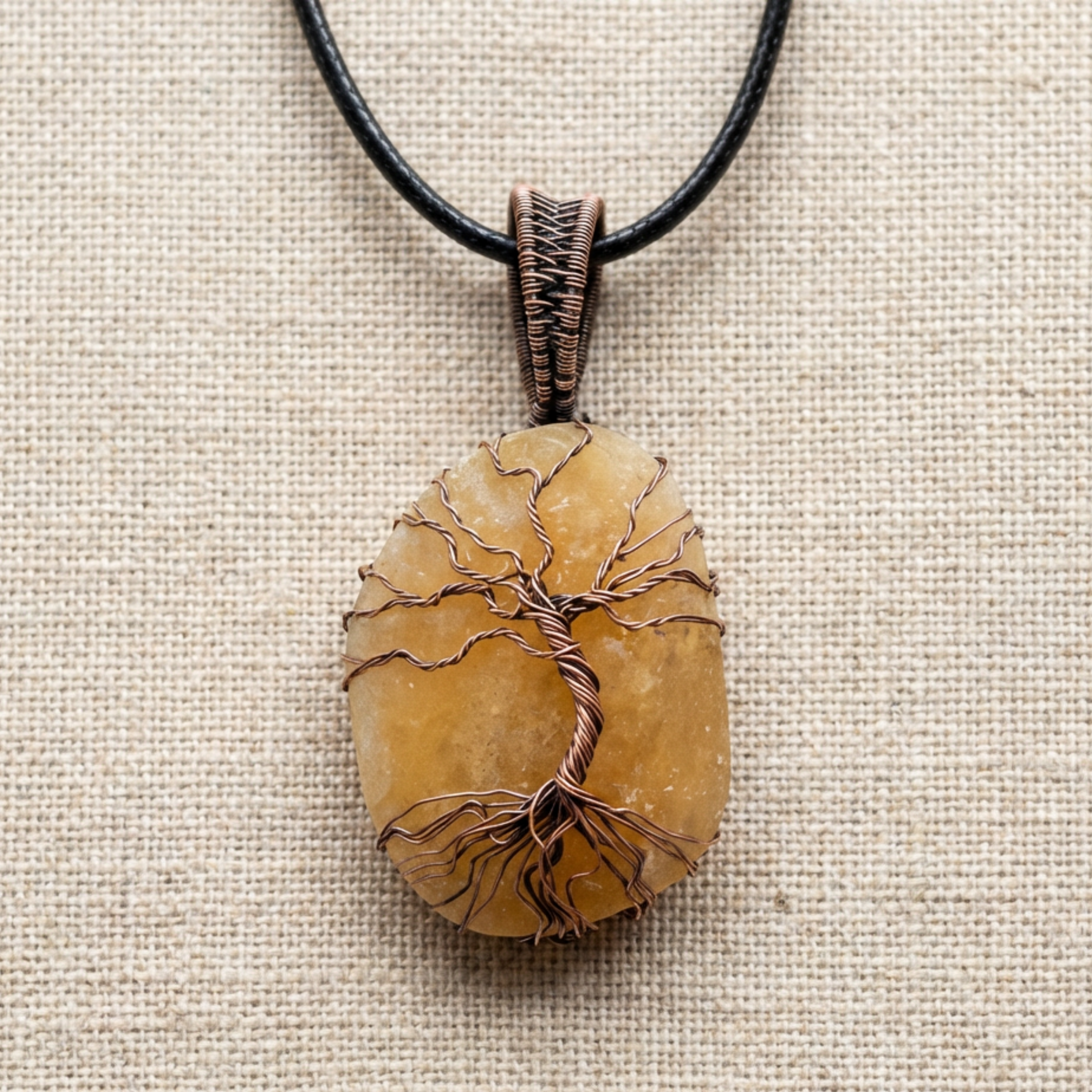 Copper Tree of Life encasing a orange calcite stone pendant on a cream fabric surface