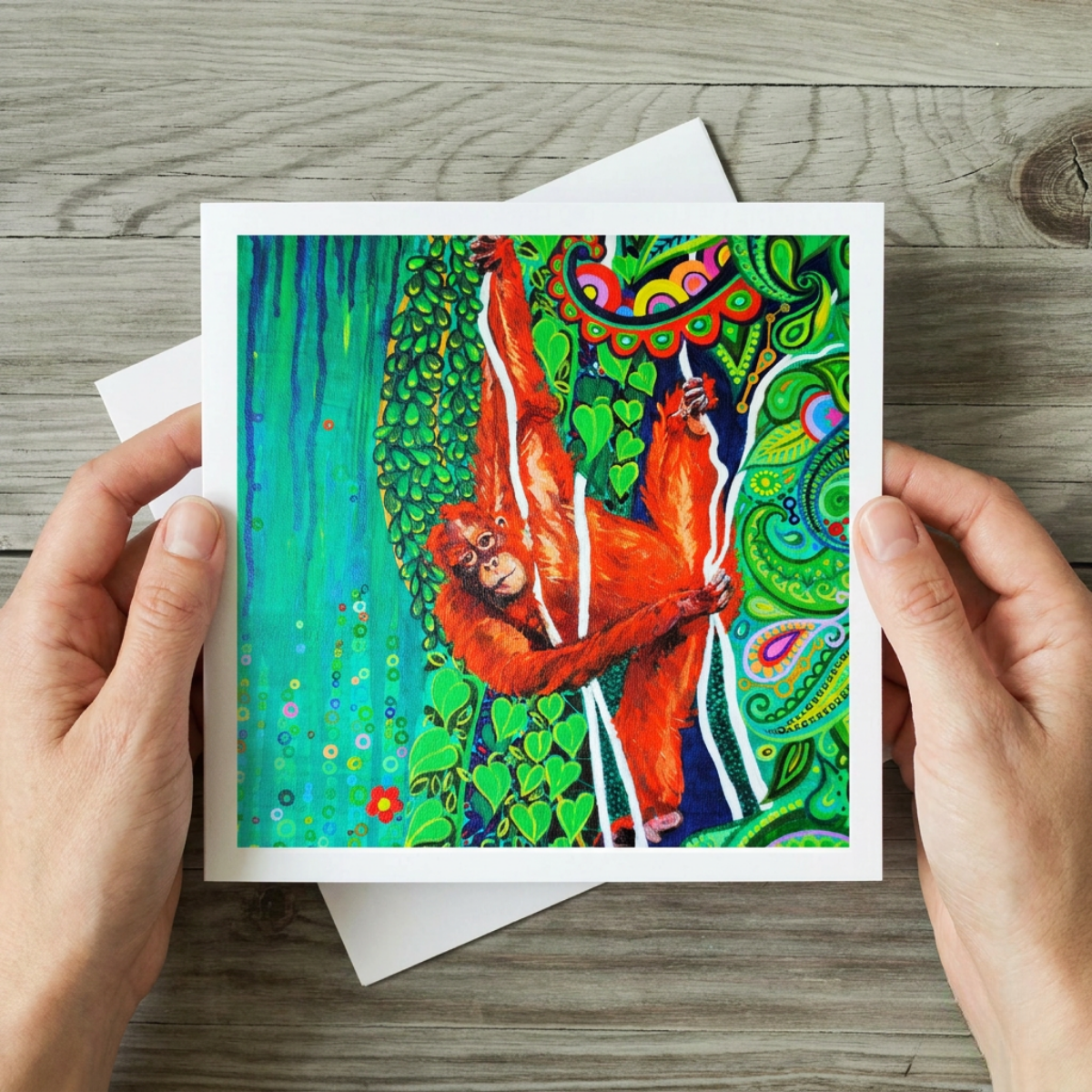 Colourful greeting card with an orangutan design held by hands on a wooden surface