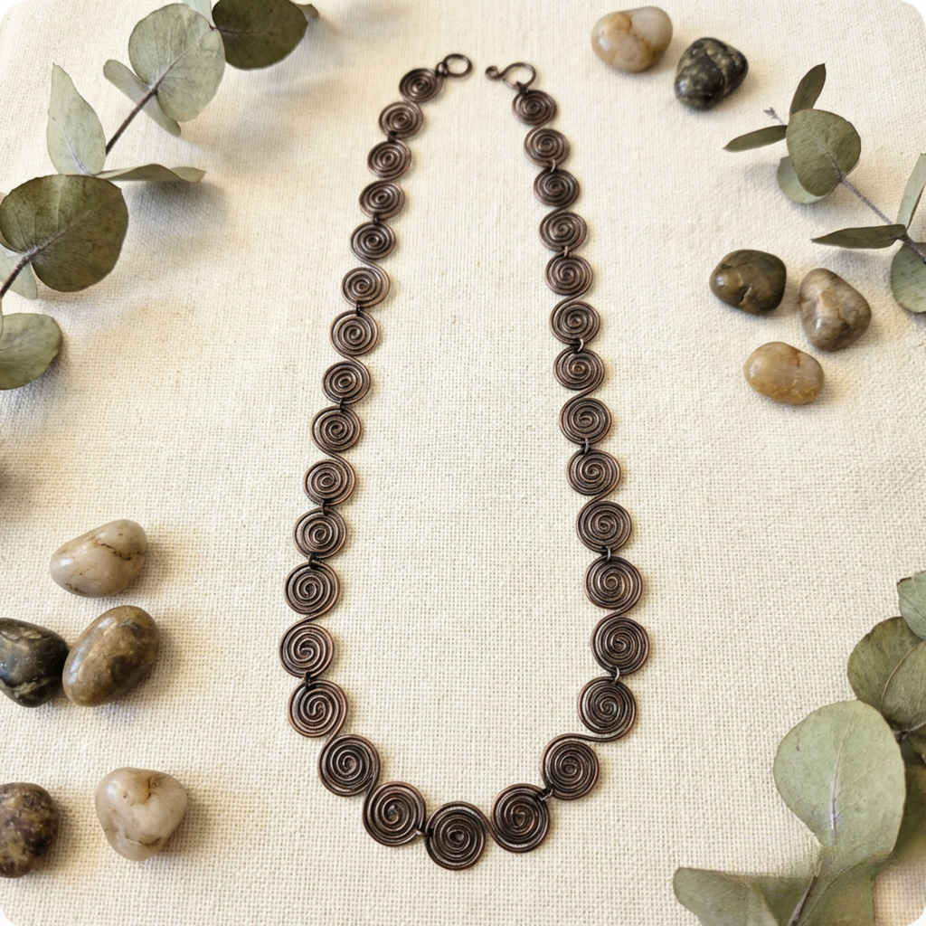 Necklace with spiral design on a textured surface with stones and leaves