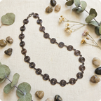 Necklace with circular spirals in copper on a textured surface with stones and eucalyptus leaves.