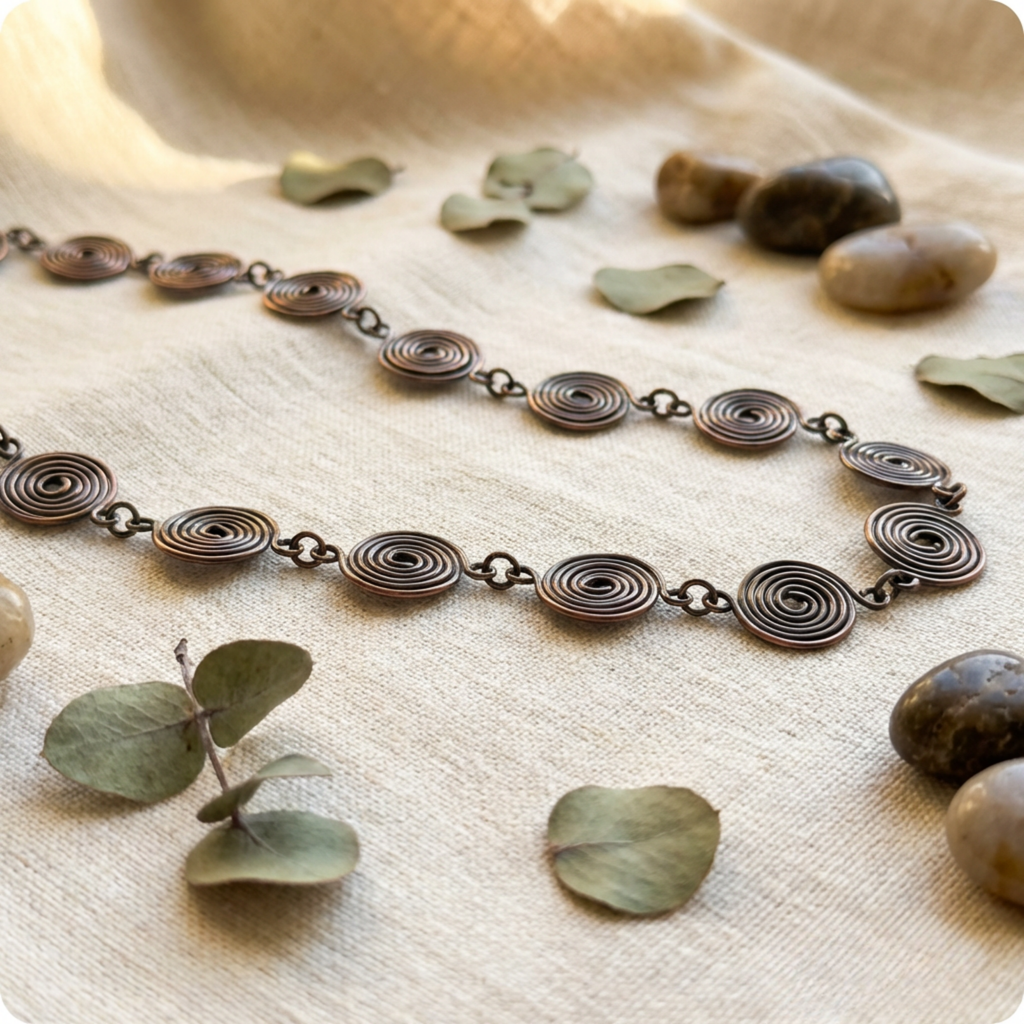 Necklace with spiral design on a textured surface with leaves and stones