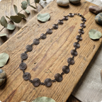 Necklace with spiral designs on a wooden surface with leaves and stones.