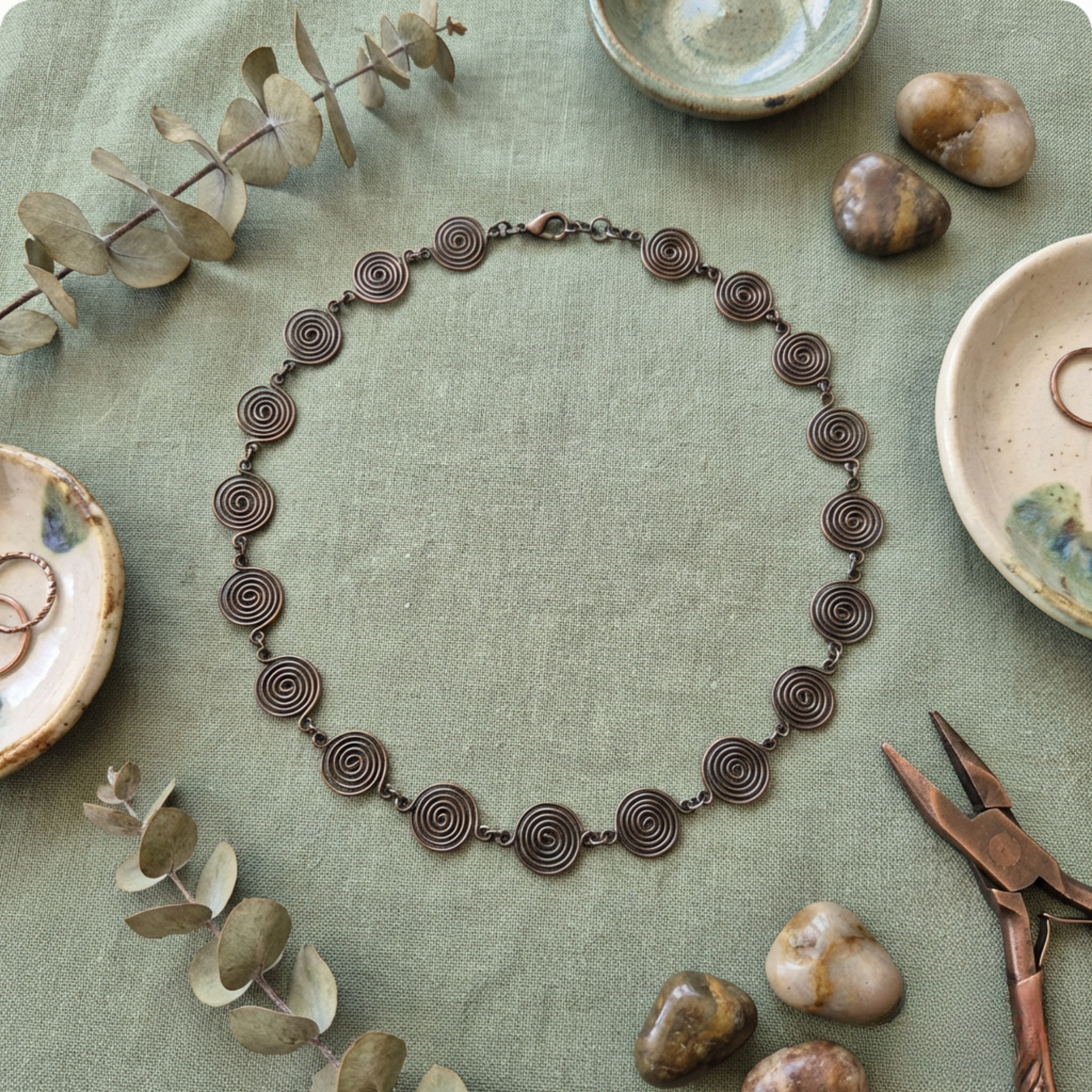 Bronzed copper spiral necklace on a textured green surface with ceramic bowls and stones