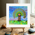 Colourful mandala abstract artwork on a small easel with decorative stones on a wooden surface.