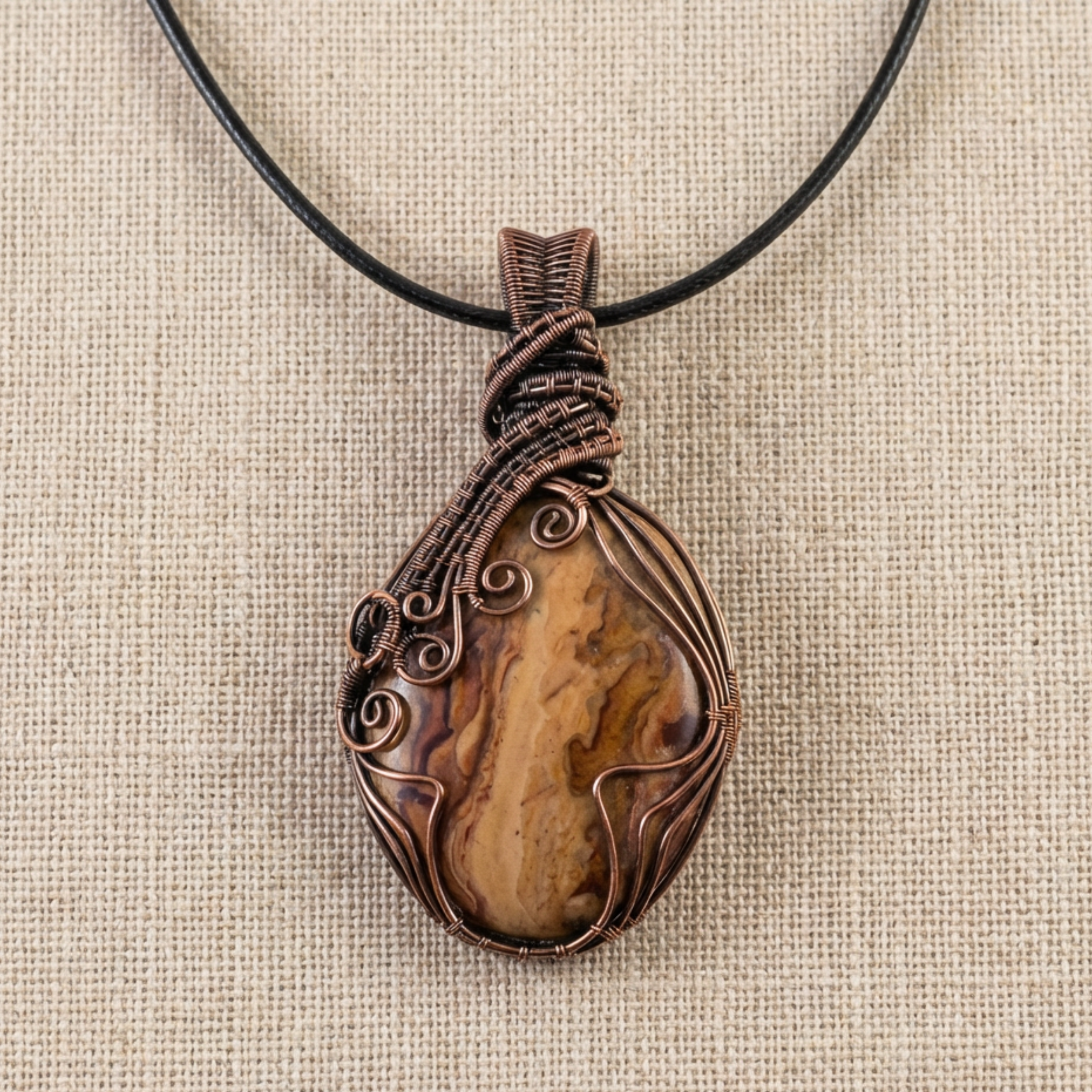 Brown stone pendant with copper wire wrapping on a beige fabric background