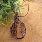 Copper pendant on a wooden surface with green leaves