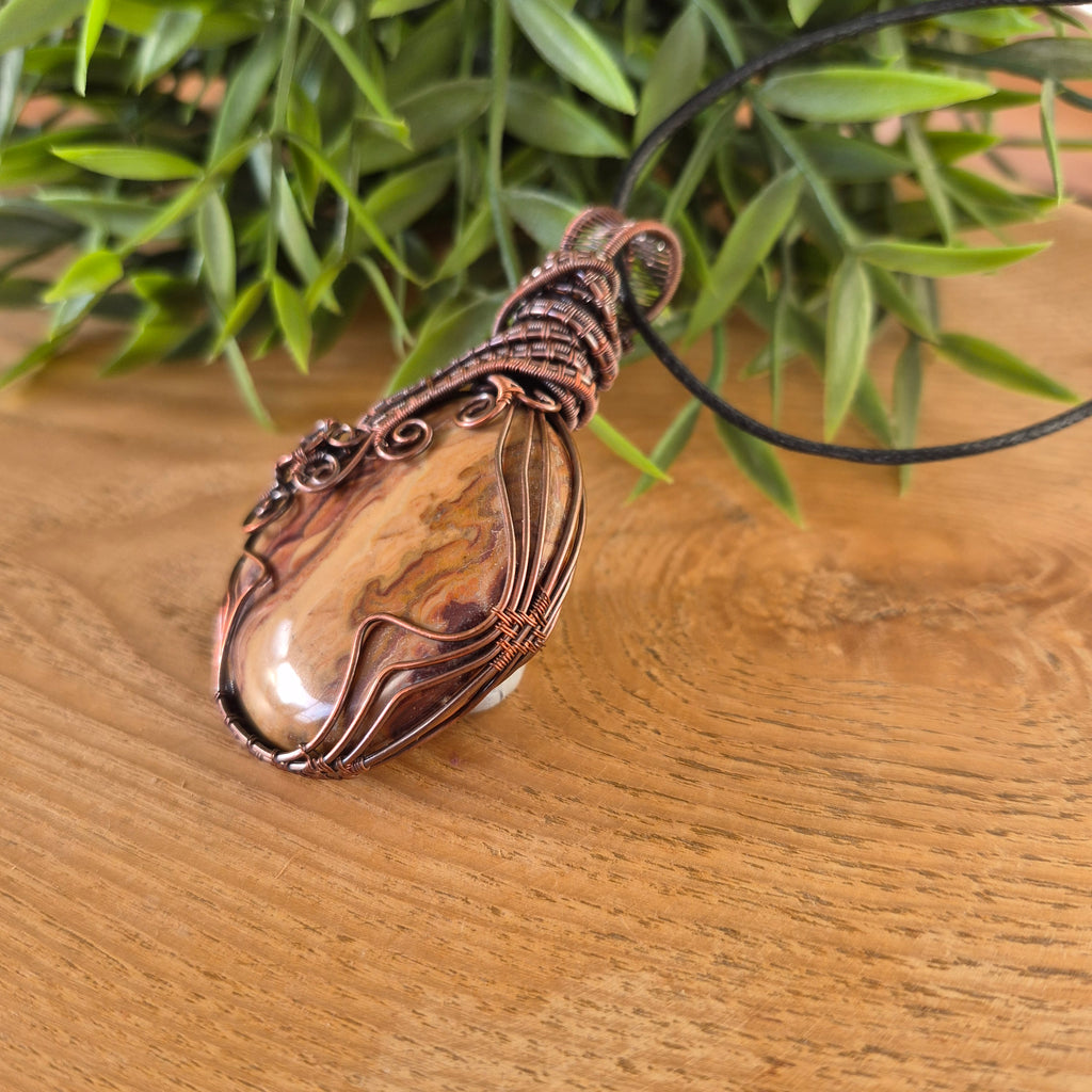Copper pendant on a black cord against a wooden background with greenery