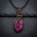Purple and pink crackle quartz agate gemstone pendant with copper wire wrapping on a dark background
