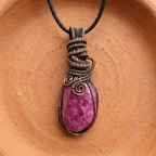 Pink stone pendant with wire wrapping on a brown surface