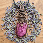 Pink stone pendant with bronzed copper wire wrapping on a wooden surface with dried lavender flowers