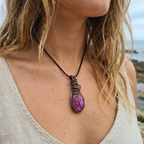 Person wearing a necklace with a purple and pink crackle quartz Agate copper wire wrapped pendant on a beach