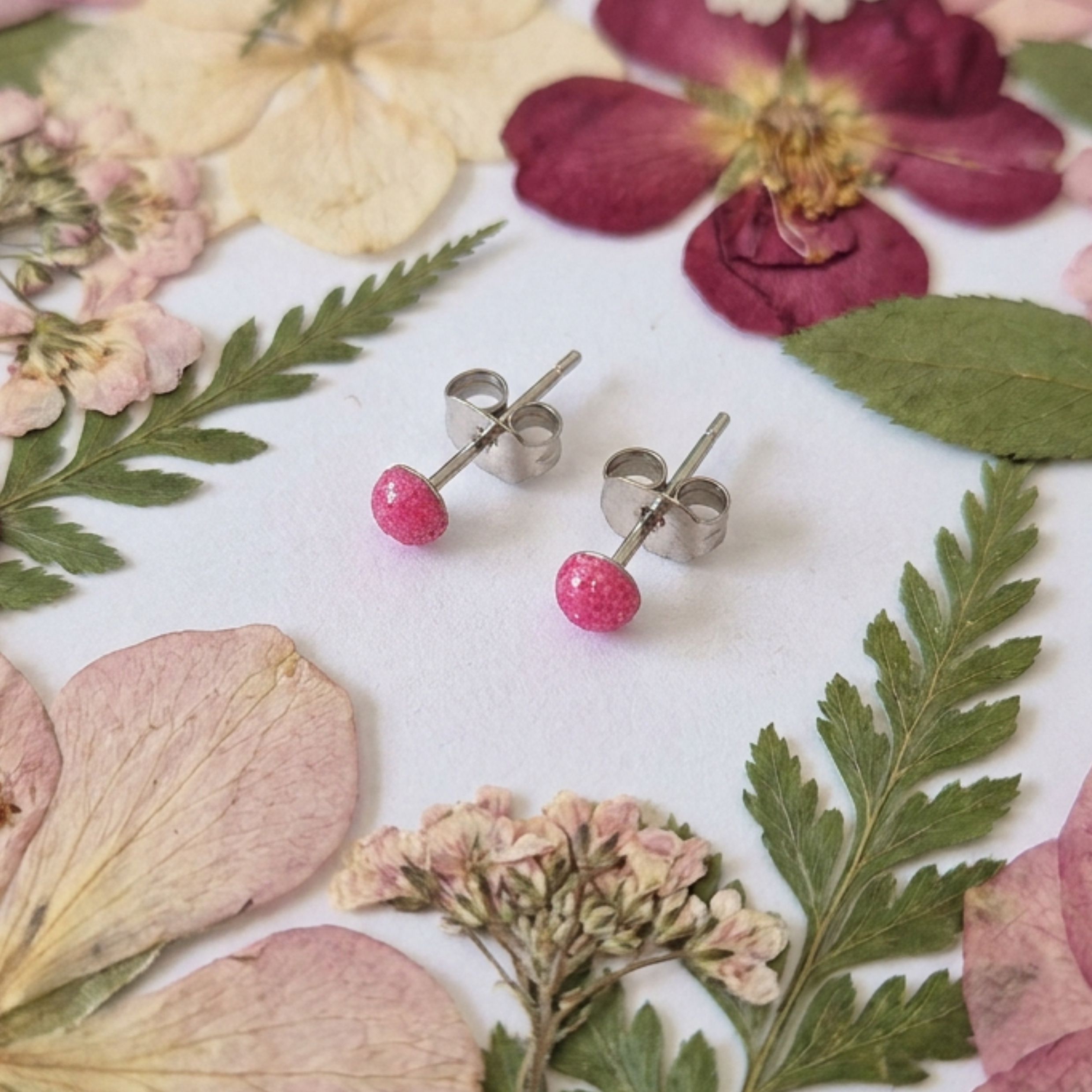 Small 3mm pink dot stud earrings on a white surface with flowers