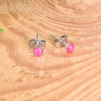 Stud earrings with 3mm pink dots on a wooden surface