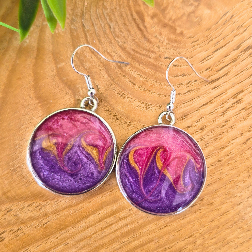 Round earrings with pink and purple design on a wooden surface