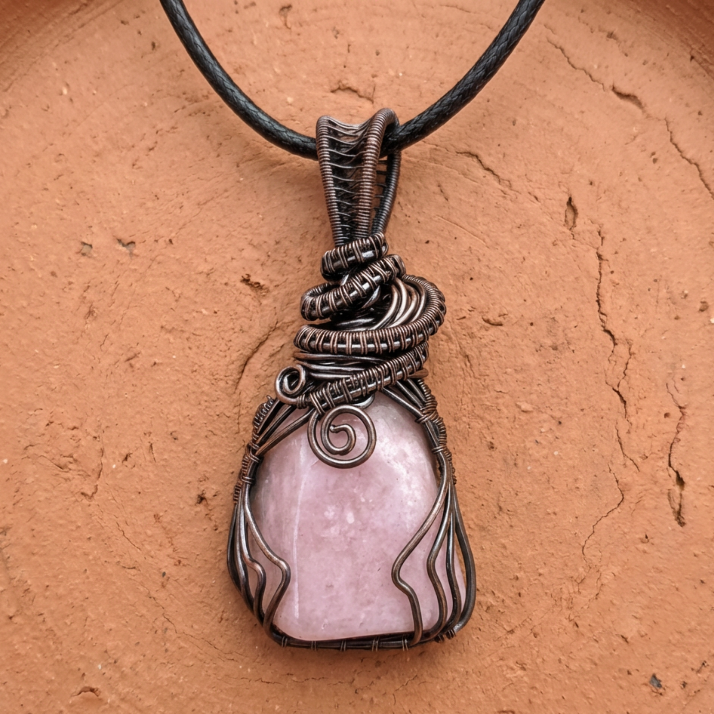 Pink stone pendant with wire wrapping on a brown background