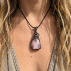 Necklace with a pink stone pendant worn by a person with long hair.