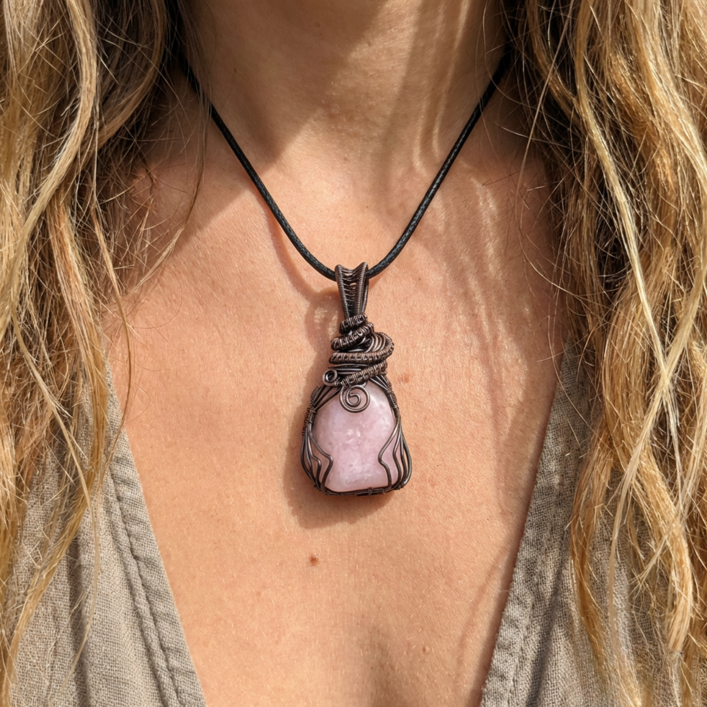 Necklace with a pink stone pendant worn by a person with long hair.