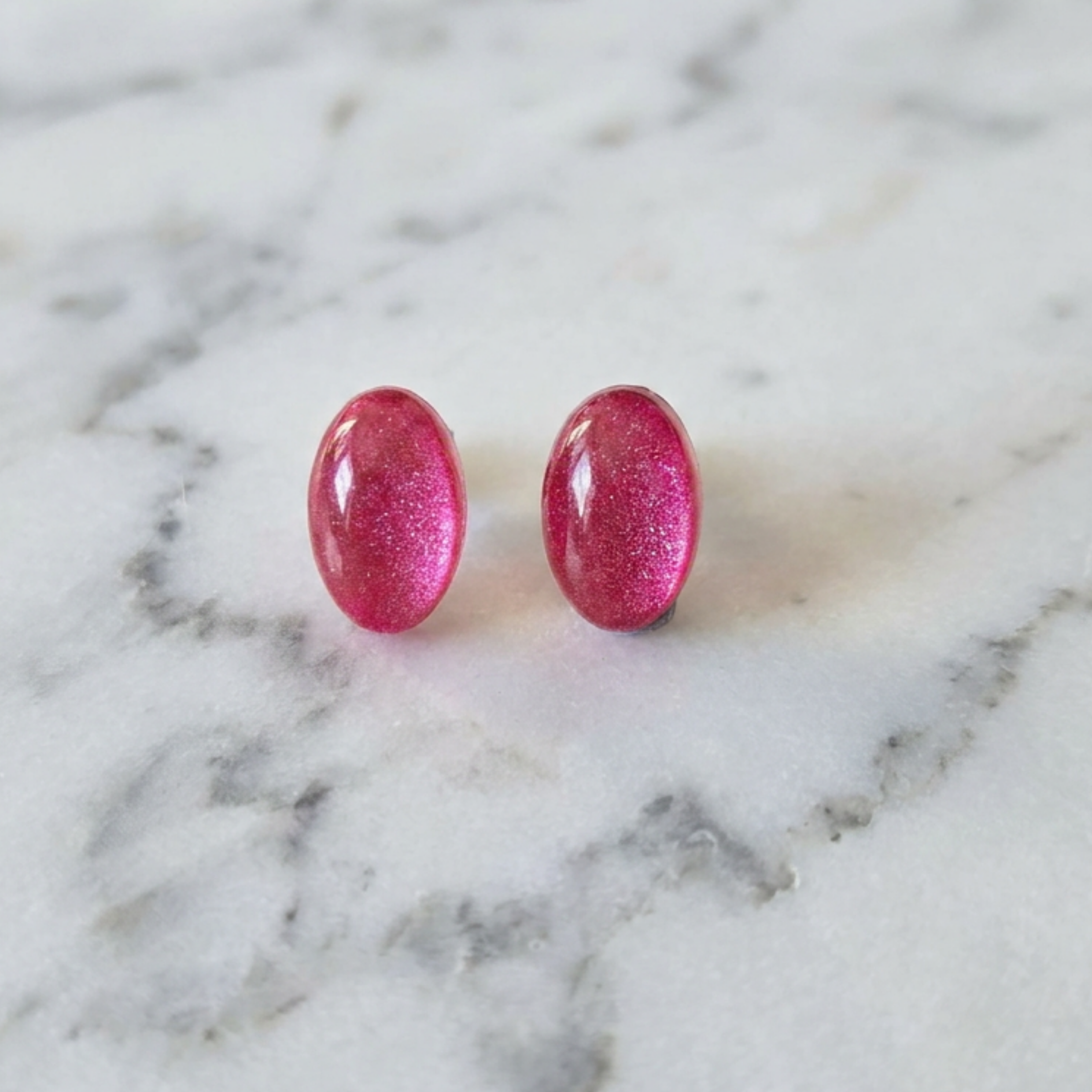 Pink glittery earrings on a marble surface